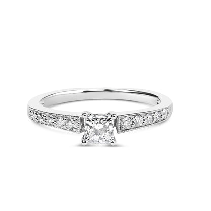 White metal ring with a princess-shaped white gemstone in a four-prong setting at center, flanked by round white gemstones in shared prong settings along the band, shown from a front angle.