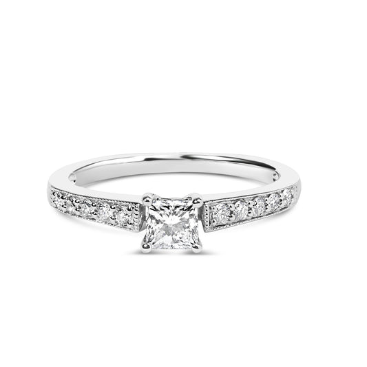 White metal ring with a princess-shaped white gemstone in a four-prong setting at center, flanked by round white gemstones in shared prong settings along the band, shown from a front angle.