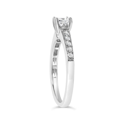 Side angle view of a white metal ring featuring a princess-shaped white gemstone in a 4-prong setting and multiple round white gemstones in a shared prong setting along the band.