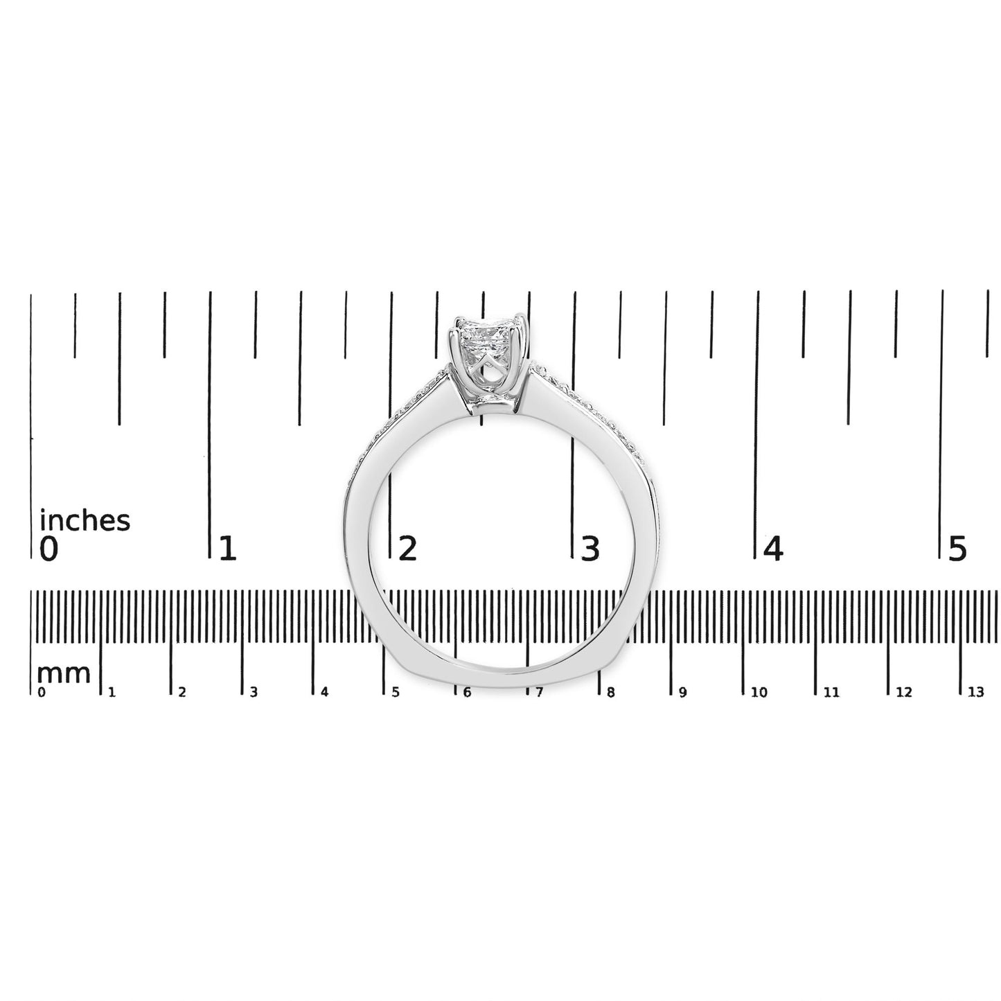 White metal ring with a princess shape gemstone in a four-prong setting flanked by round gemstones in a shared prong setting, shown from the side on a ruler for size reference.