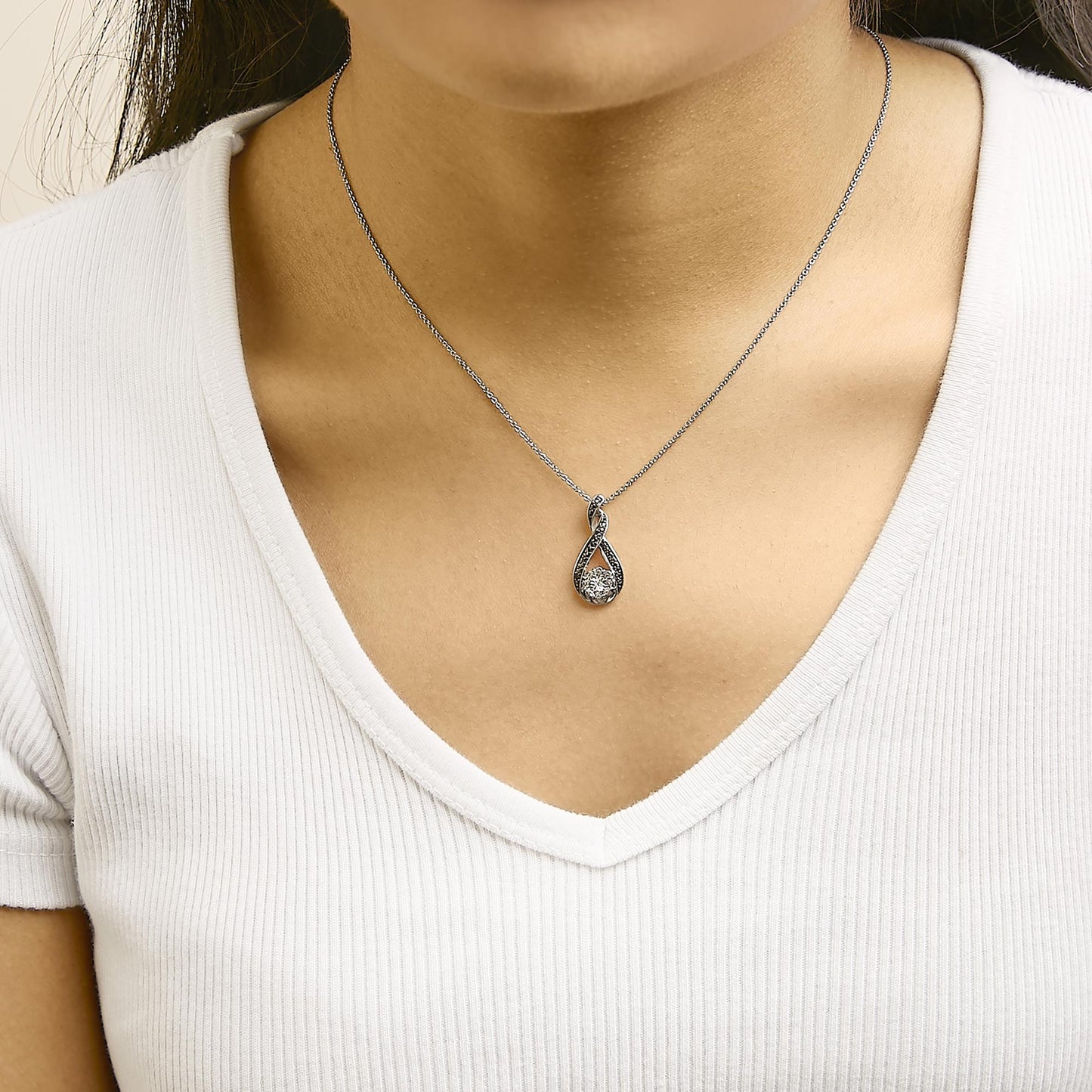 Necklace with a white and black metal twisted teardrop pendant featuring a central white gemstone and small black gemstones in pave setting, worn on a model shown from the front.