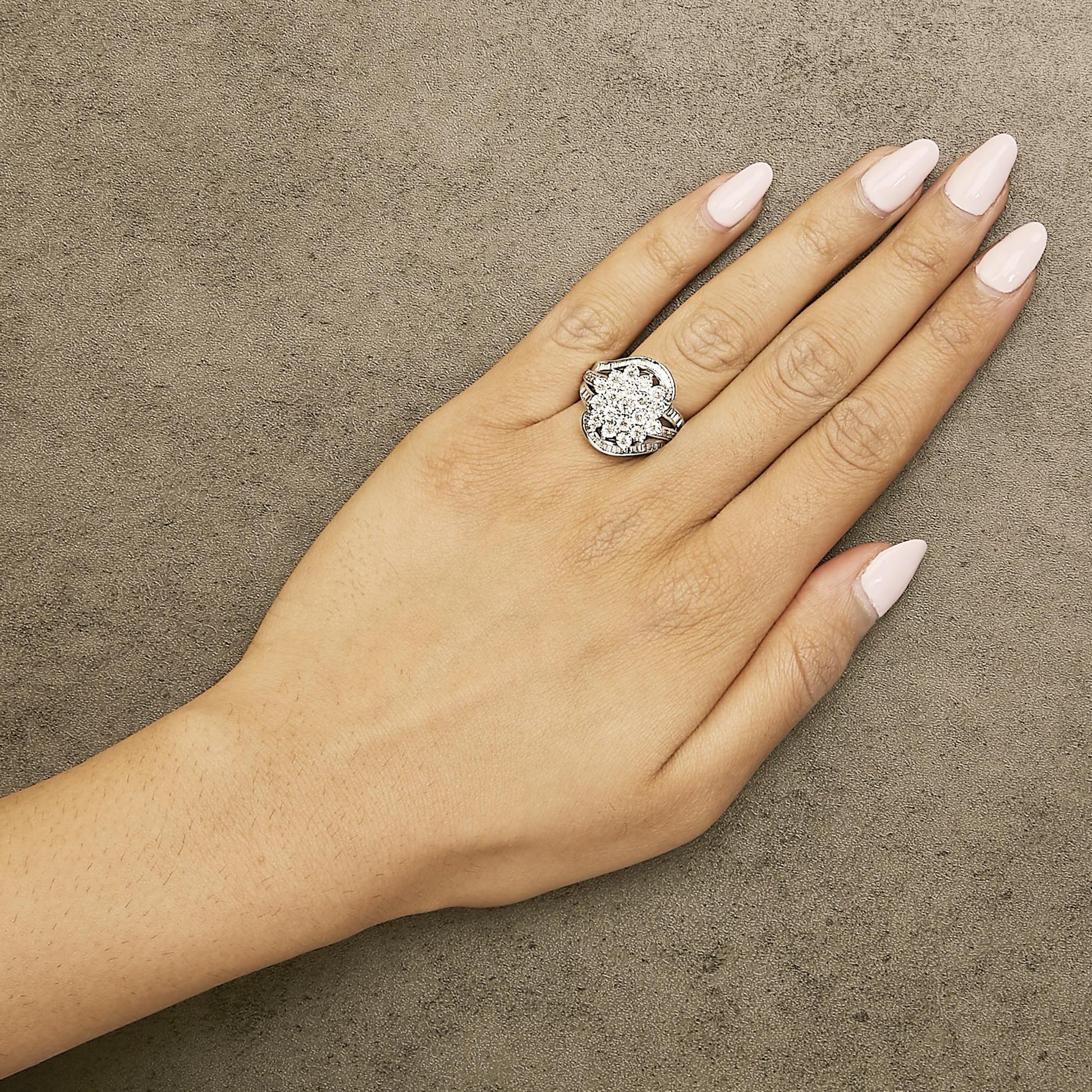 White metal ring with a cluster of round and baguette white gemstones, worn on a model's hand, shown from above at a slight angle.