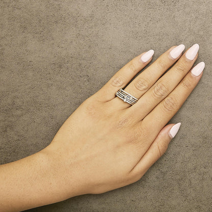 Close-up top view of a hand model wearing a white metal ring set featuring round white gemstones in bezel and prong settings.