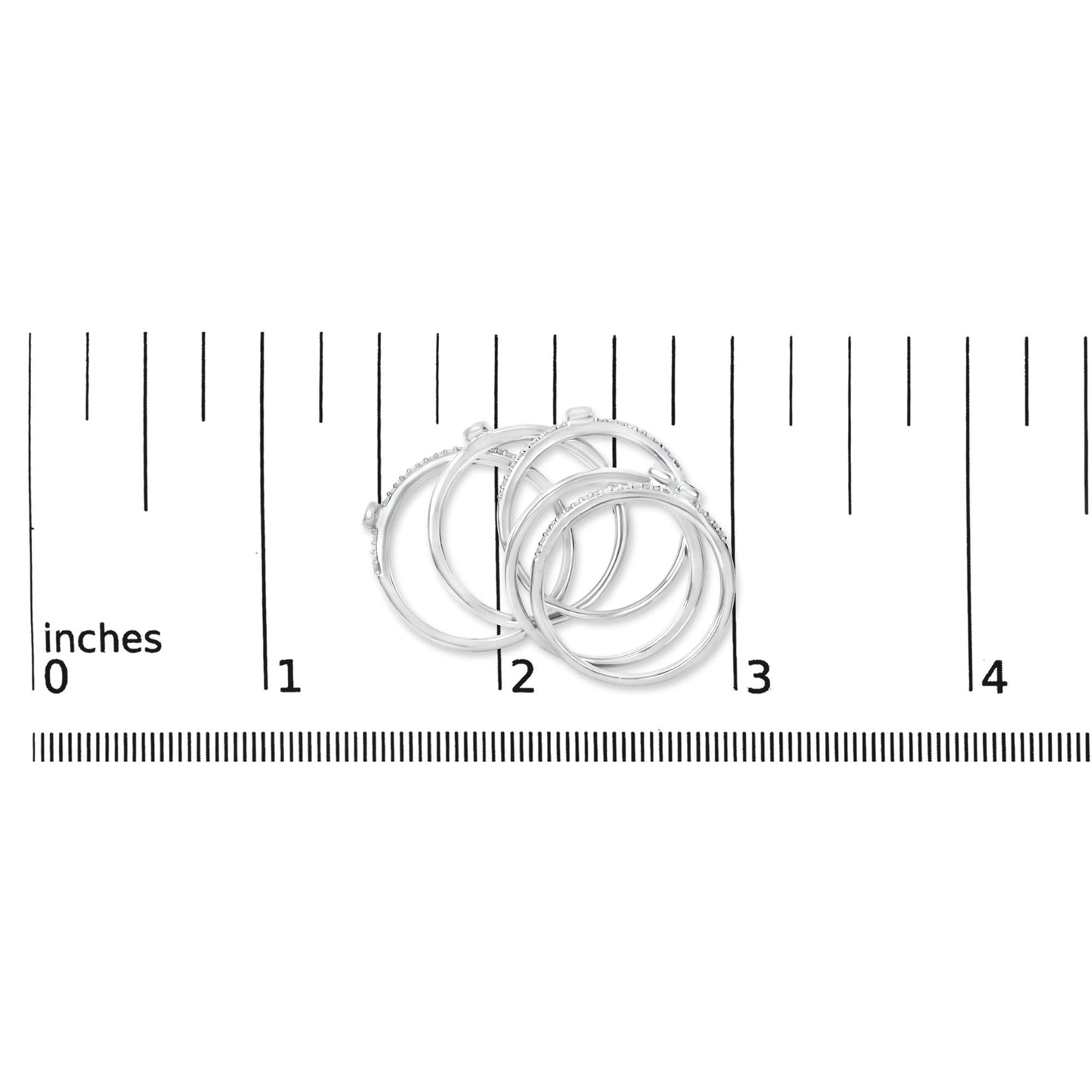 Close-up front angle of four white rings with small round white gemstones in bezel and prong settings, shown on a ruler scale.