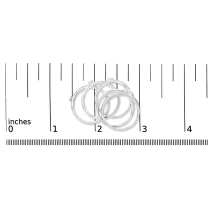 Close-up front angle of four white rings with small round white gemstones in bezel and prong settings, shown on a ruler scale.