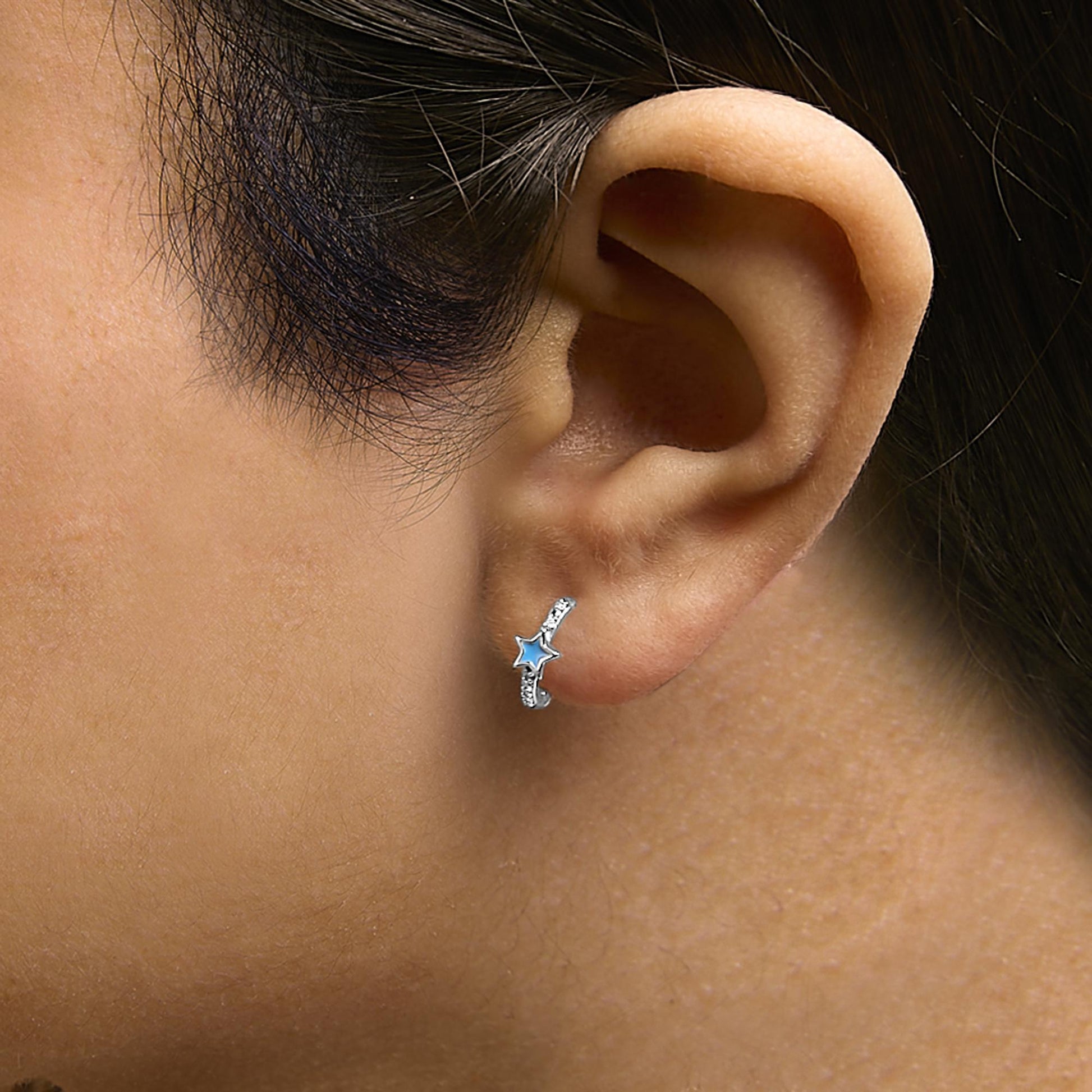 Close-up side view of a model wearing a white hoop earring featuring a star-shaped blue gemstone and round white gemstones in a pave setting.