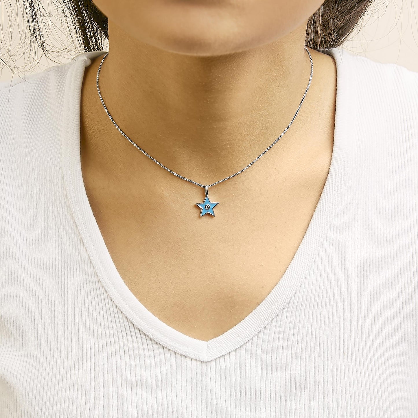 Close-up front view of a model wearing a white metal necklace with a star-shaped pendant featuring a blue detail and a round white gemstone set in the center.