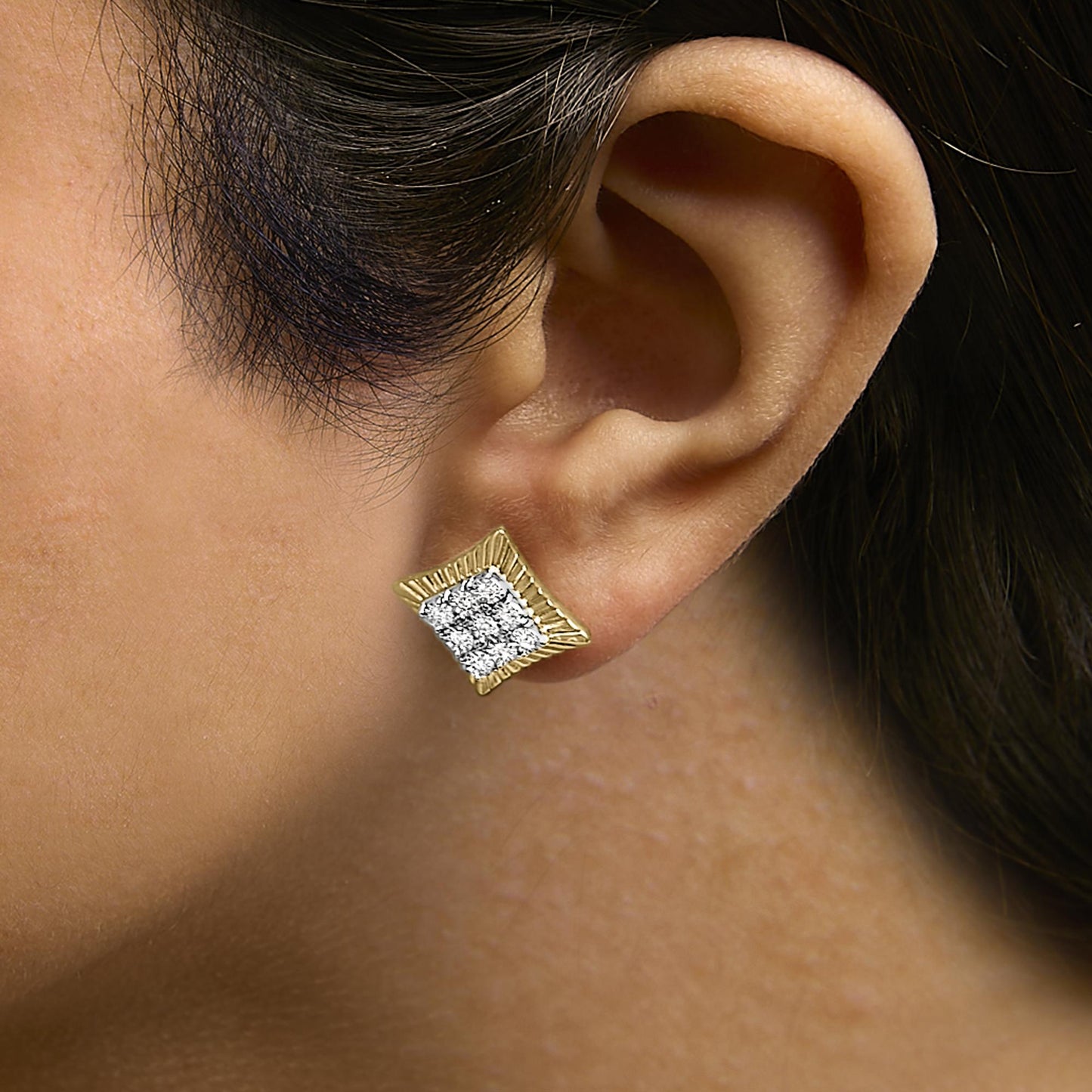 Close-up side view of a model wearing a square-shaped earring with a yellow metal frame and multiple small white round gemstones in bezel settings in the center.