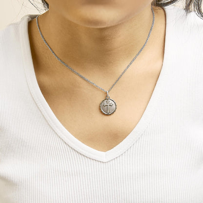 Necklace worn on model showing a round pendant with a cross design featuring white pave-set round gemstones on a yellow and white metal chain, front center close-up angle.