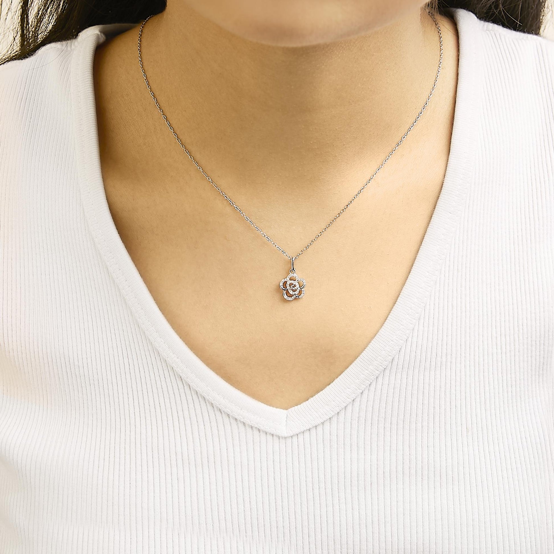 Necklace with a white metal chain and a flower-shaped pendant adorned with round white gemstones shown worn on a model, front-facing angle.
