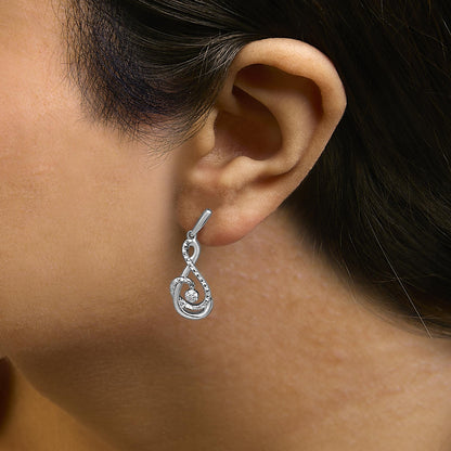 White metal earrings with a looping, abstract swirl design set with small white round gemstones in prong settings, shown worn on a model's ear in a close-up side profile shot.