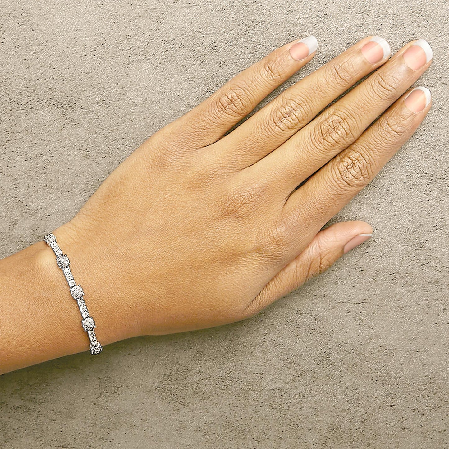White metal bracelet with round white gemstones in prong setting, shown on a model's wrist from a top-down angle.