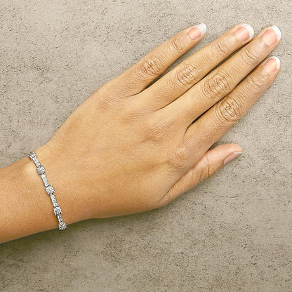 White metal bracelet with round white gemstones in prong setting, shown on a model's wrist from a top-down angle.