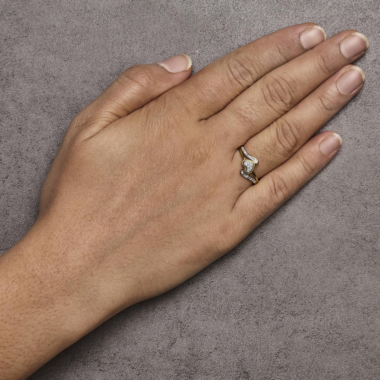 Close-up top view of a hand wearing a yellow and white metal ring with white round pave-set gemstones, featuring a central heart shape flanked by curved bands with gemstones.