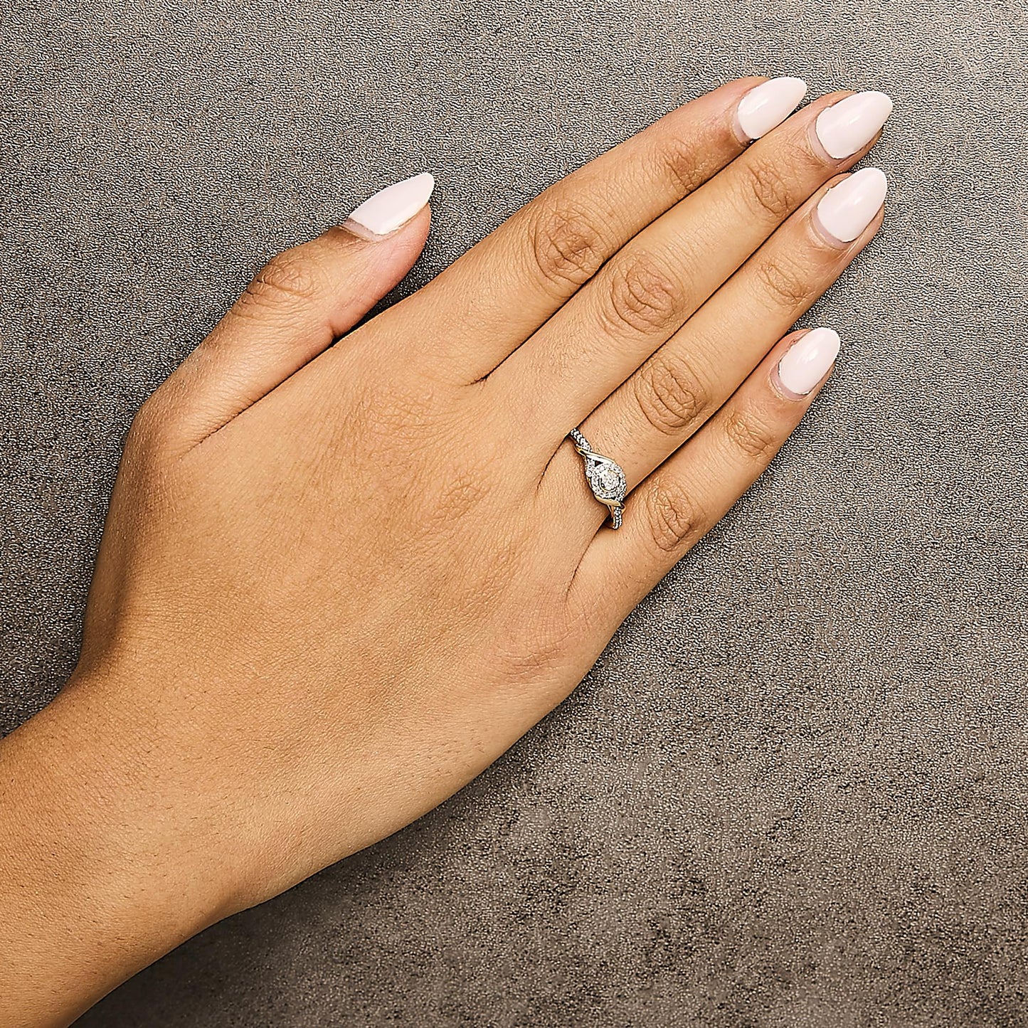 Yellow metal ring with a twisted design and round white gemstones in prong settings, shown worn on a model's hand from a top-down angle.