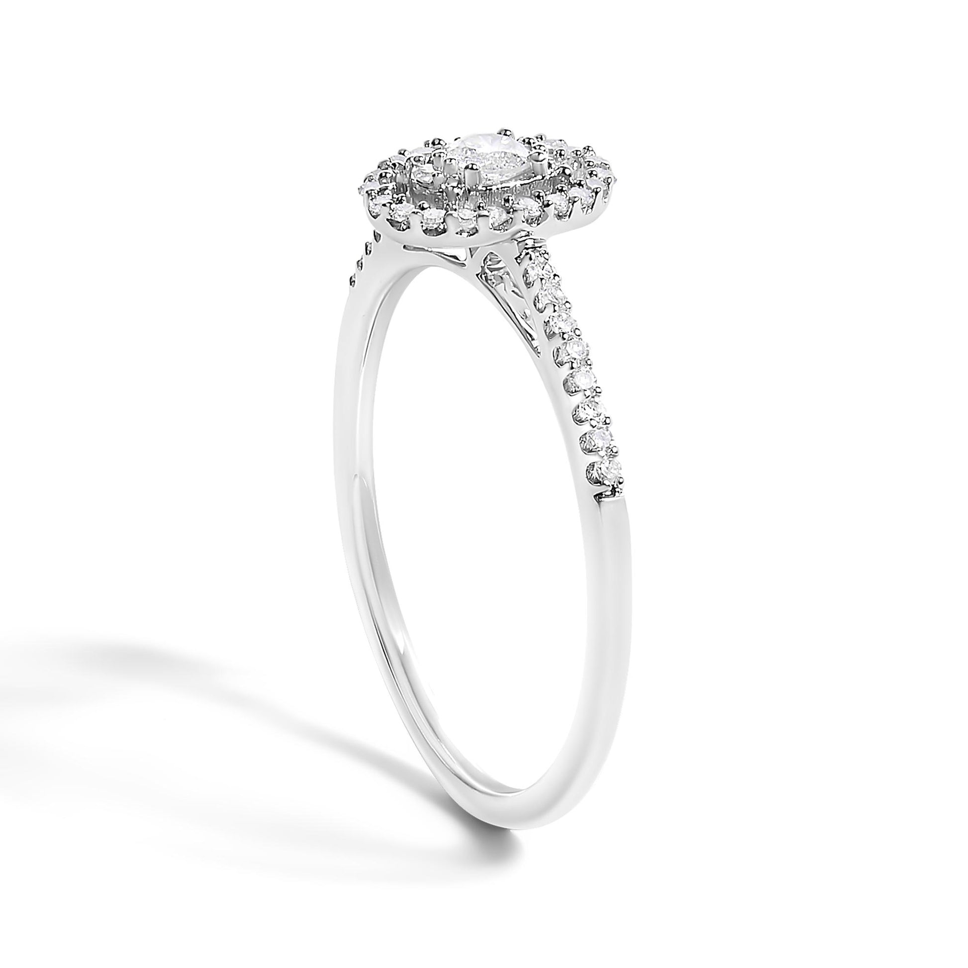 White metal ring with a round center white gemstone in prong setting, surrounded by smaller white gemstones in prong settings on a halo and along the upper band, shown from a side angle.