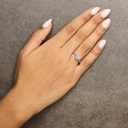 White metal ring with a central round white gemstone surrounded by smaller white gemstones in a halo setting, shown worn on a model's hand, angled from above.