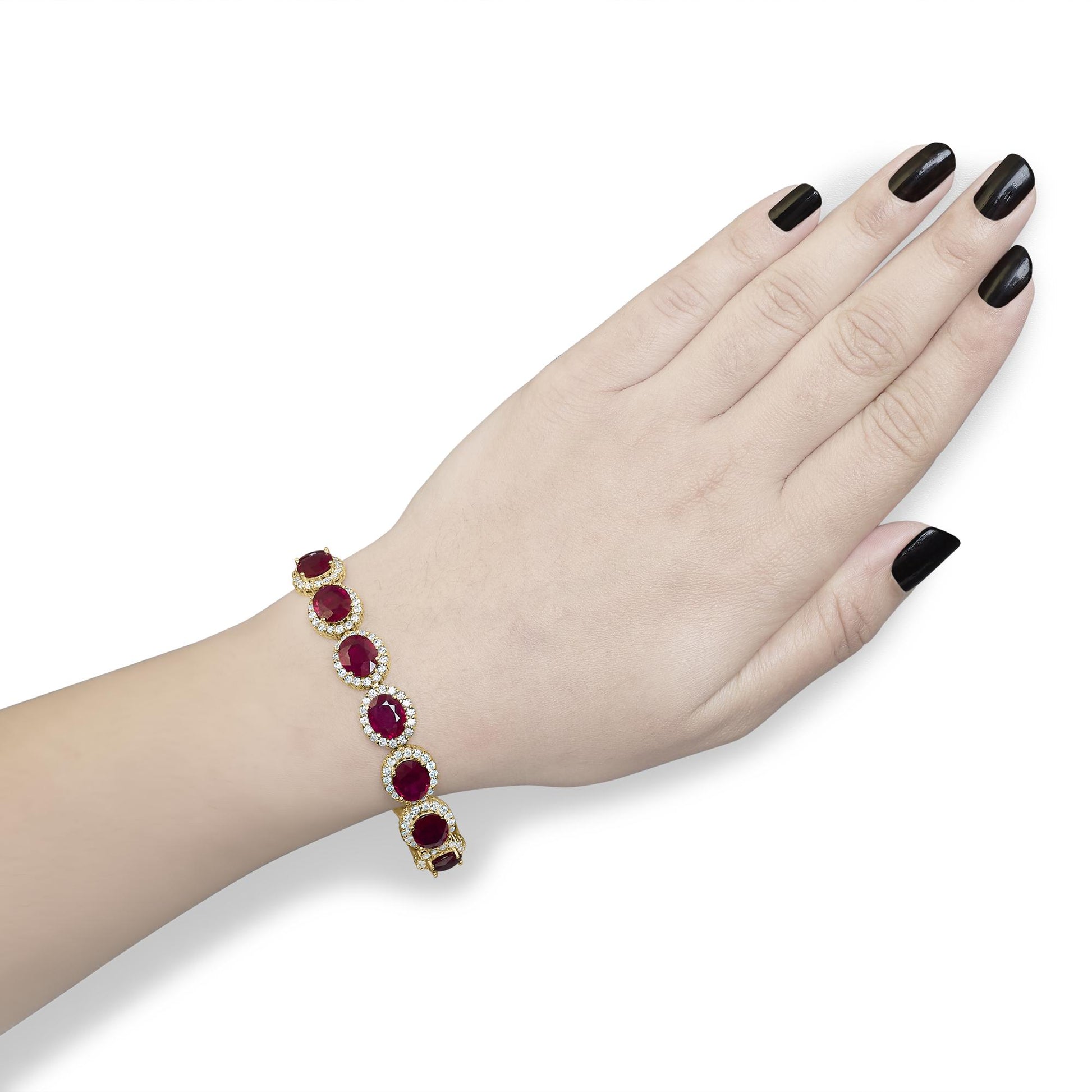 Yellow metal bracelet with oval red gemstones surrounded by small round white gemstones, shown on a model's wrist from a top angle.