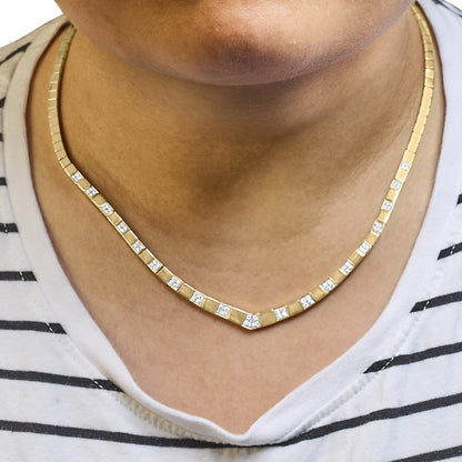 Close-up front view of yellow metal necklace with square links and multiple white round gemstones worn on a model's neck.