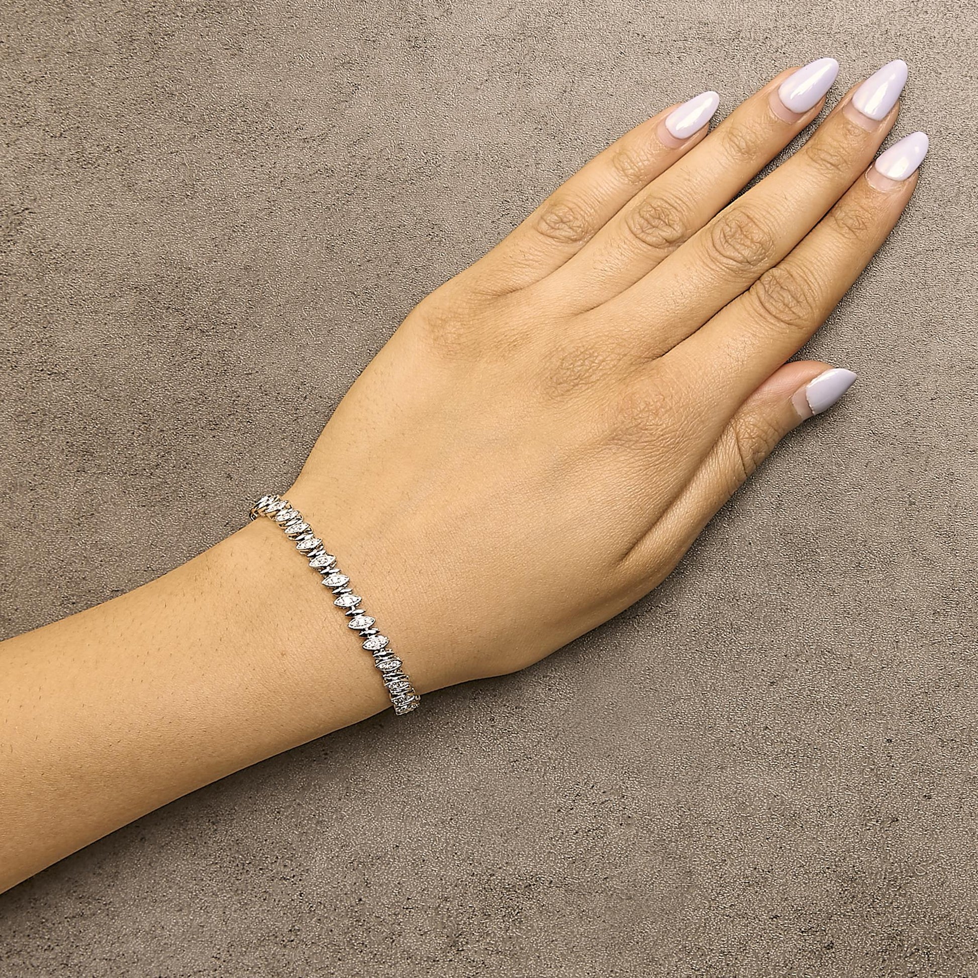 White metal bracelet with round pave-set white gemstones, shown worn on a model's wrist, top-down angle.