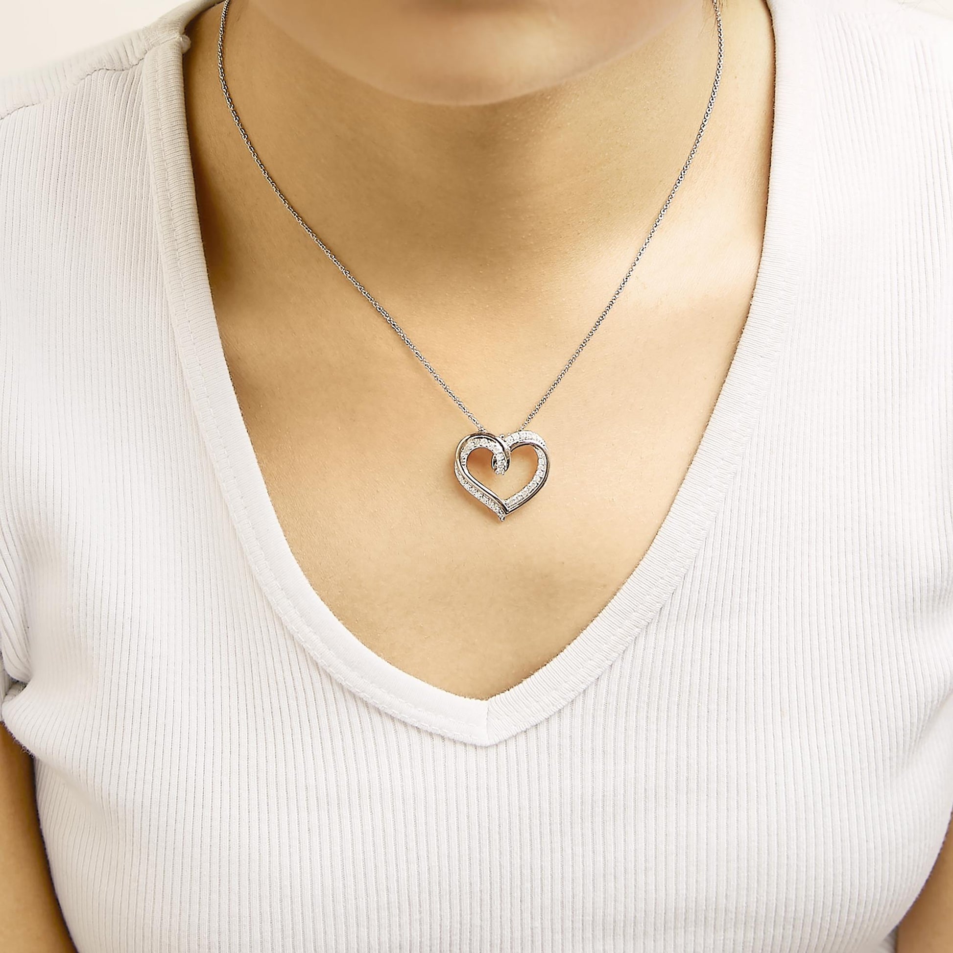 Close-up front view of a model wearing a white and rose metal heart-shaped necklace with round-shaped white gemstones set in prongs along the pendant.