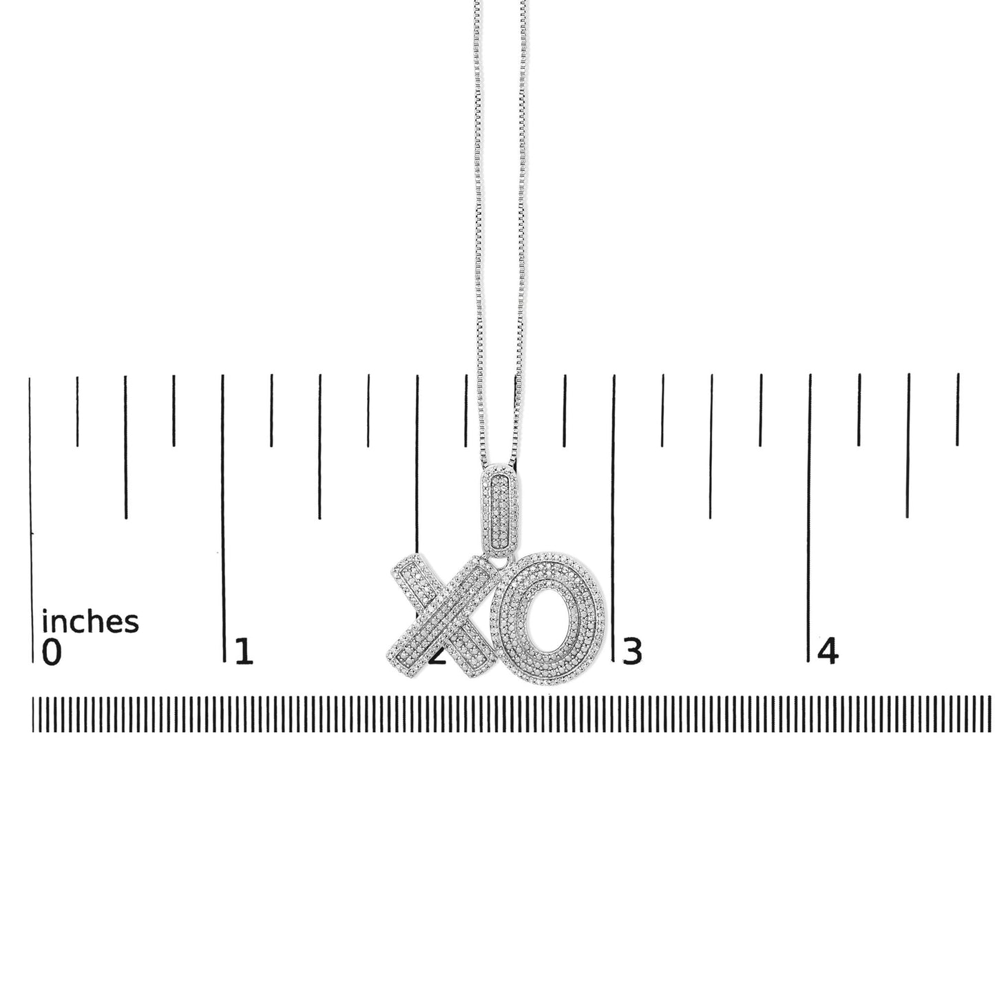 Close-up front view of a white metal necklace pendant with 'XO' letters adorned with round white gemstones in prong settings, shown on a ruler scale.