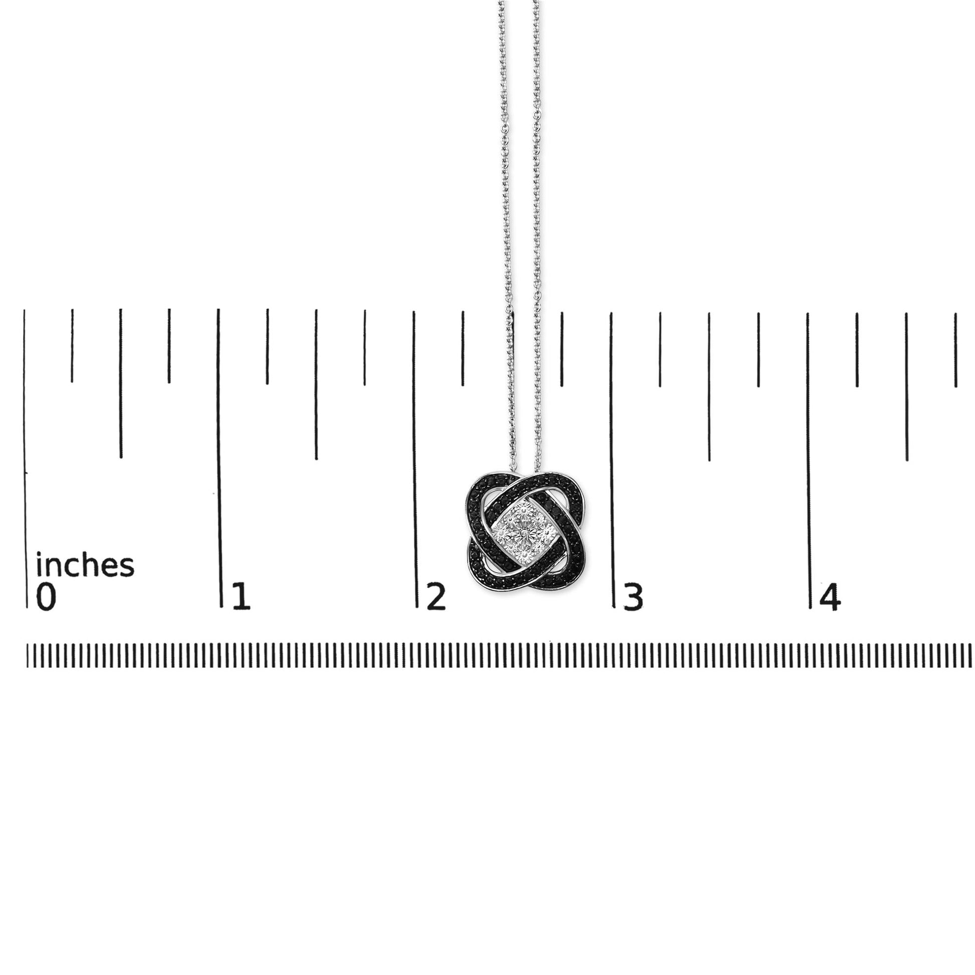 White and black metal necklace with a pendant featuring a knot shape set with one white gemstone and multiple small black gemstones, shown on a scale from a front angle.