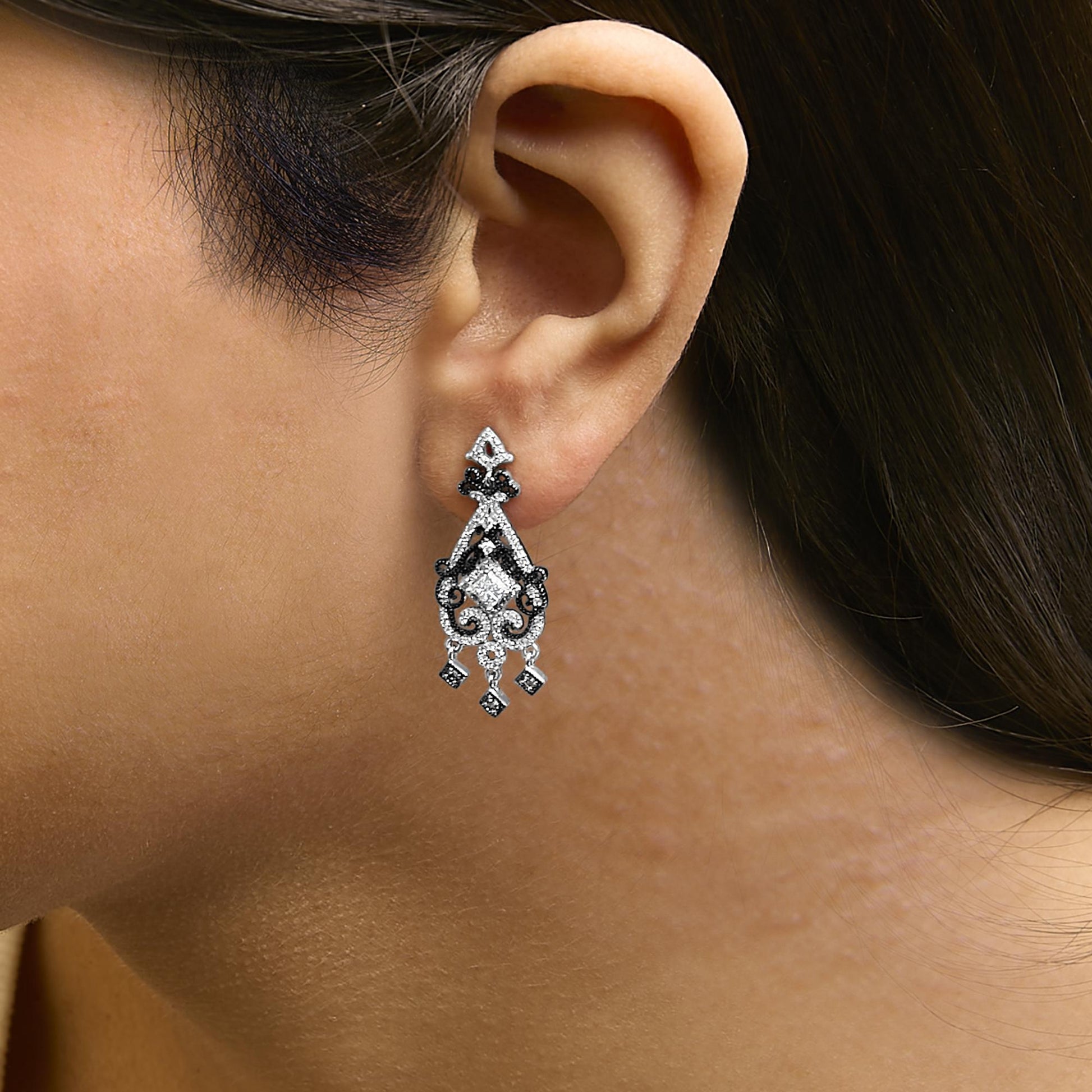 Close-up side view of a model wearing white and black metal chandelier earrings with princess-shaped, round, and other round prong-set white gemstones.