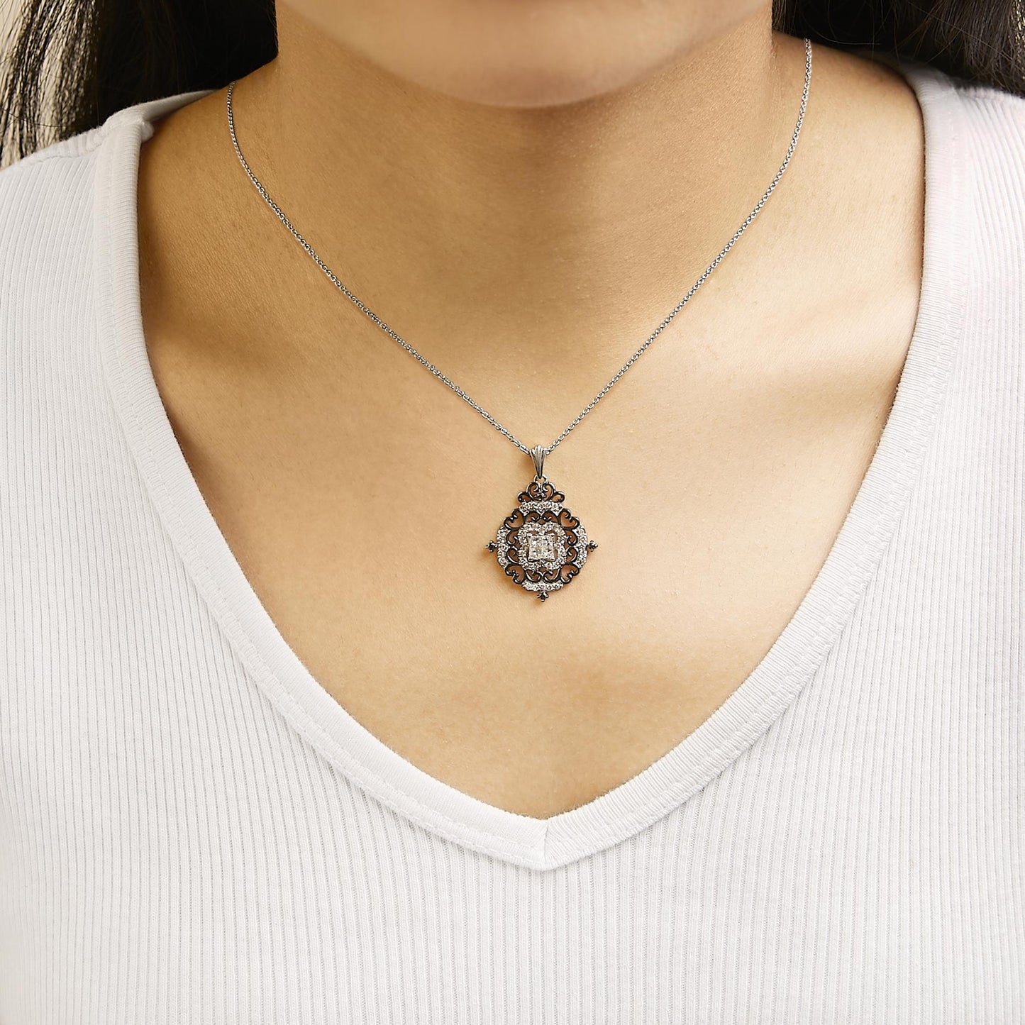 Necklace shown worn on a model, featuring a white and black metal pendant with an ornate design surrounding four white princess-shaped gemstones in the center and black round gemstones decoratively placed, shot from the front.