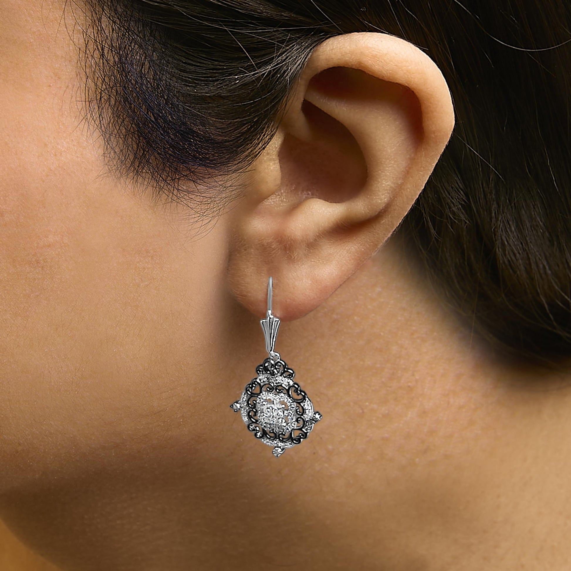 Earrings shown worn on a model, featuring a white and black metal drop design with round black gemstones in prong settings, white princess-shaped gemstones in invisible settings, and multiple small round white gemstones in shared prong settings, photographed from the side.