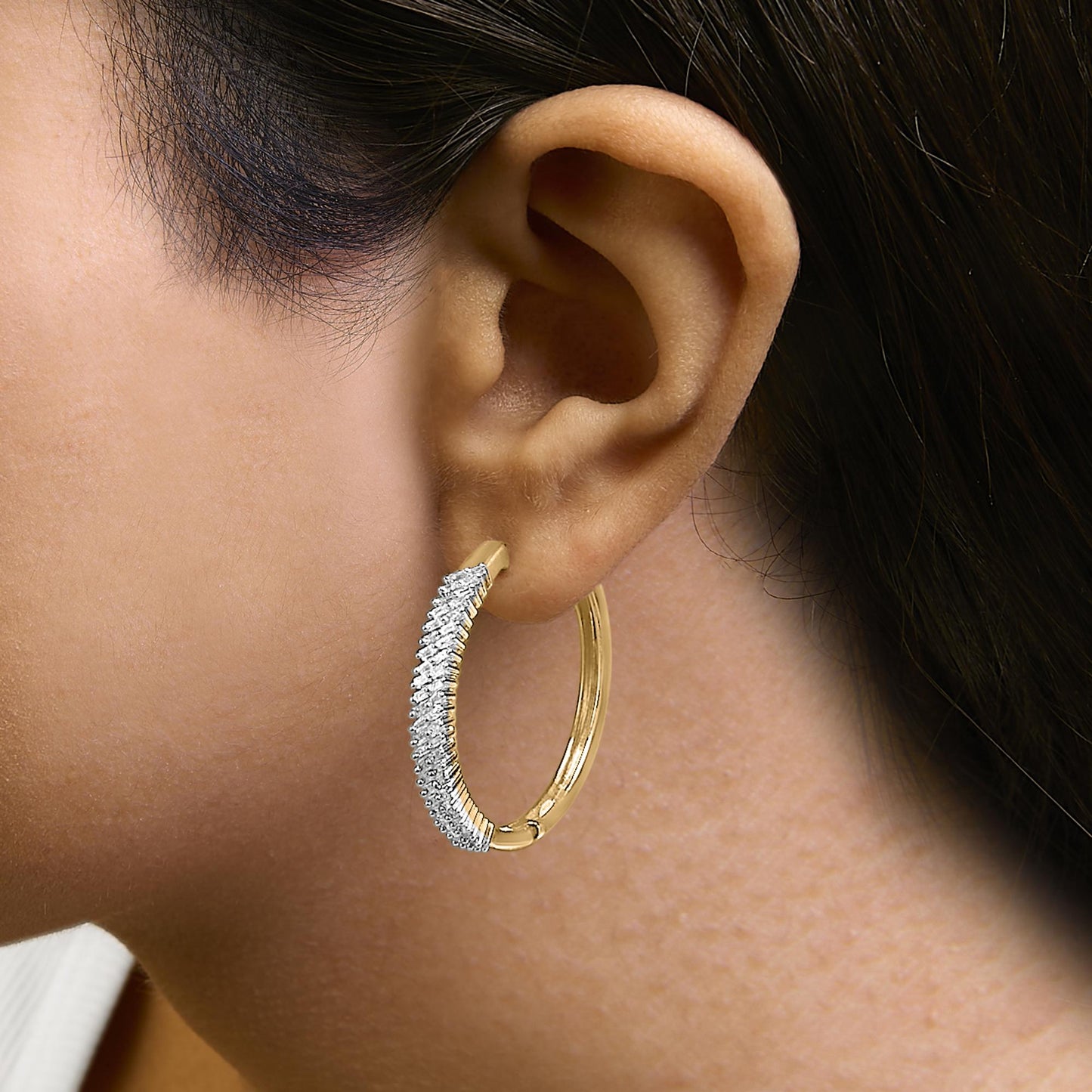 Close-up side view of a woman's ear wearing a yellow and white metal hoop earring partially encrusted with baguette-shaped white gemstones in prong settings.