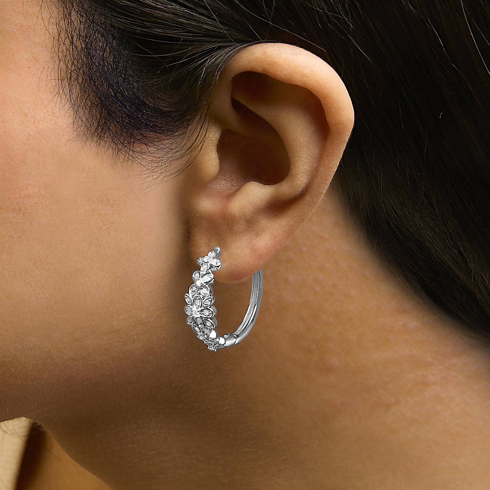 Close-up side view of a white hoop earring worn by a model, featuring a floral design with round white gemstones in a pave setting on the front half.