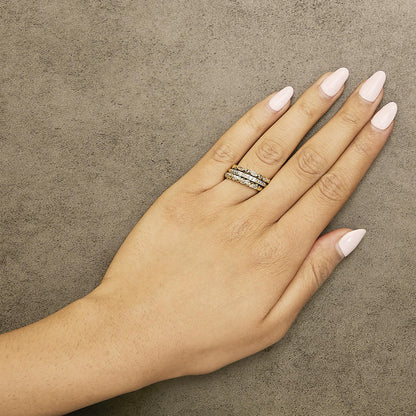 Close-up of a model's hand wearing three stacked rings in yellow and white tones, each featuring round white gemstones in pave settings, shown from above on a textured surface.