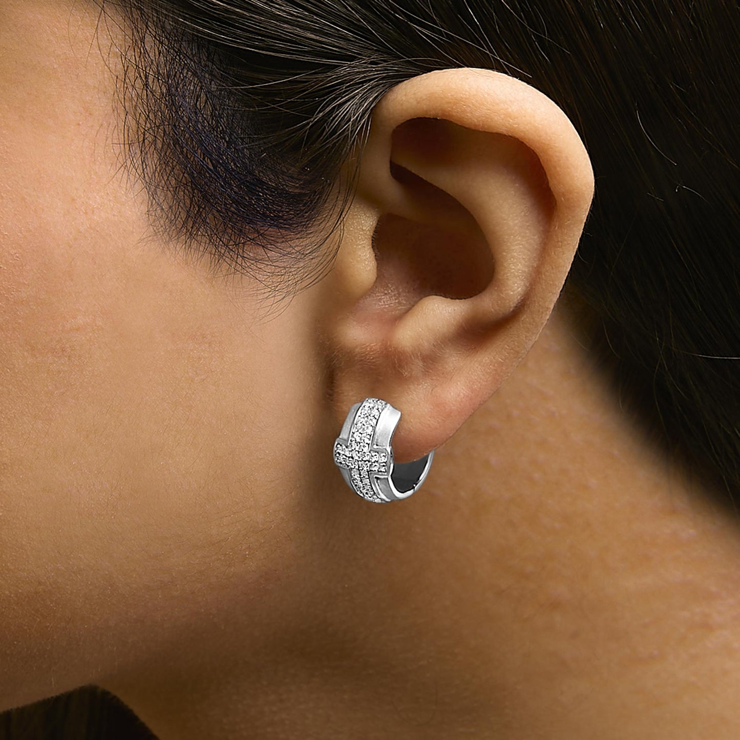 Close-up side view of a model wearing a white metal hoop earring with a crisscross design featuring round white gemstones in a pave setting.