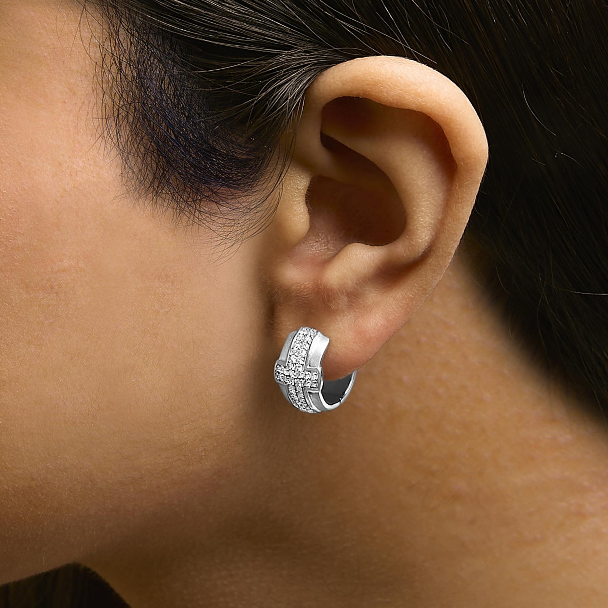 Close-up side view of a model wearing a white metal hoop earring with a crisscross design featuring round white gemstones in a pave setting.