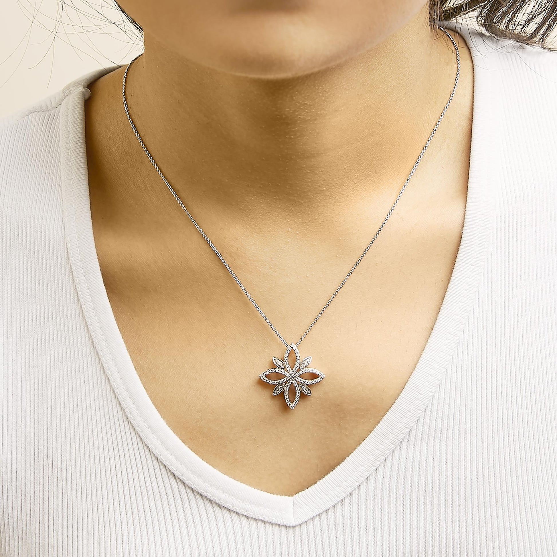 Close-up front view of a model wearing a white metal necklace with a flower-shaped pendant adorned with round white gemstones in prong settings.