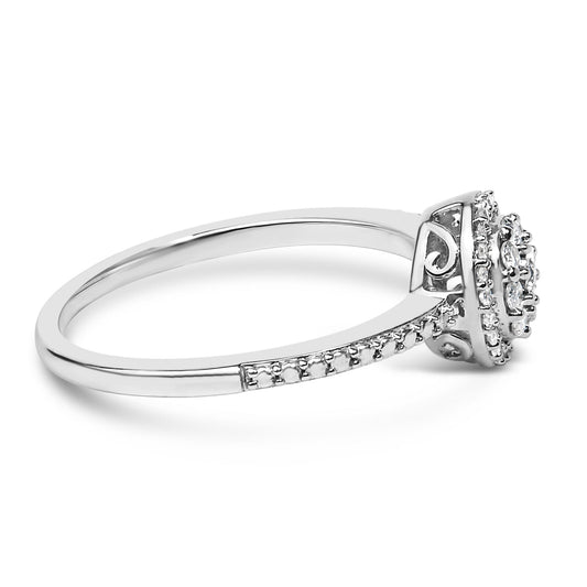 Side angle view of a white metal ring with round white gemstones in a prong setting along the band and around a raised central cluster.