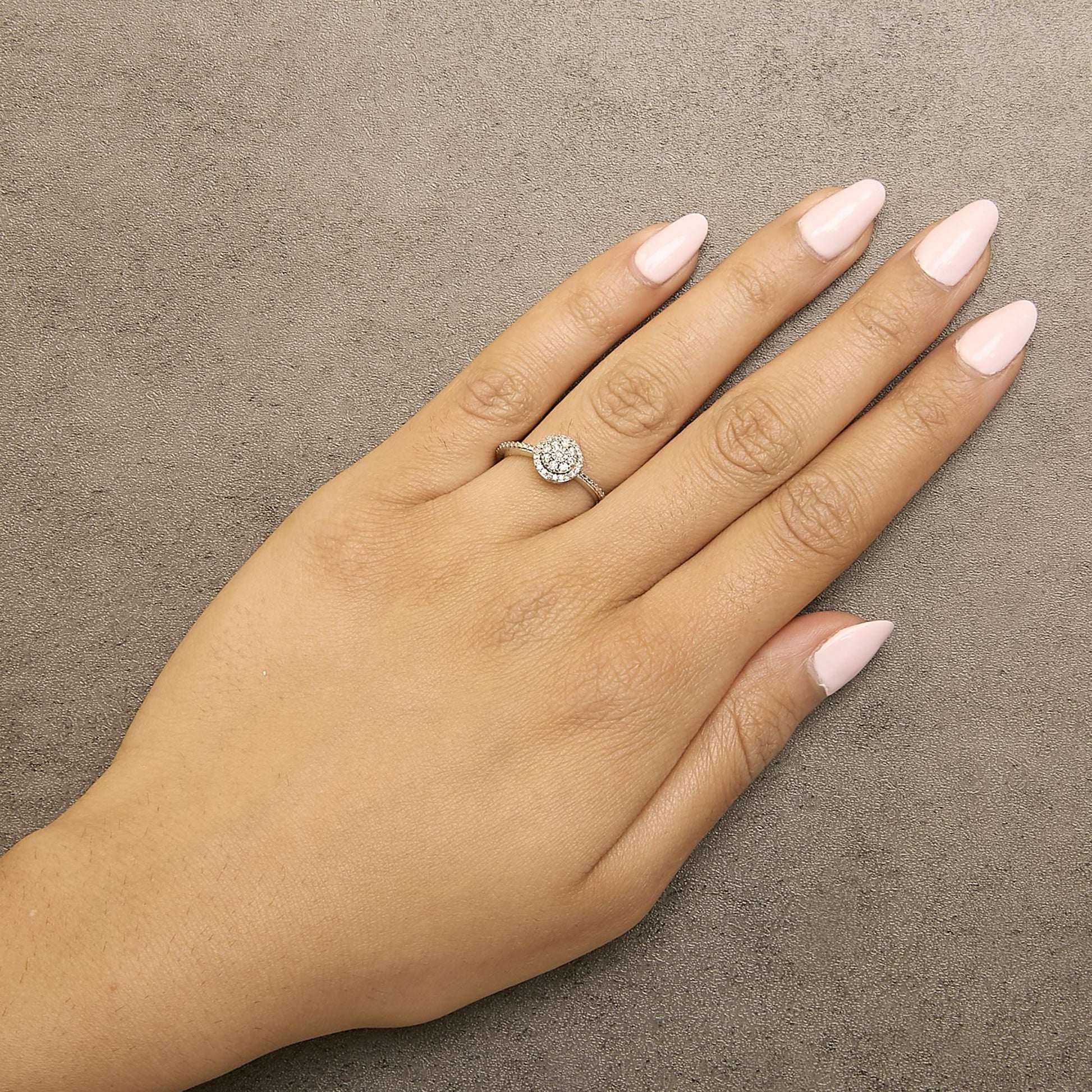 White metal ring with round white gemstones in prong setting forming a circular cluster, shown worn on a model hand from a top-down angle.