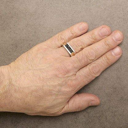 Ring with yellow, white, and black metal bands featuring three black round gemstones in a channel setting, shown worn on a model's finger from a top-down angle.