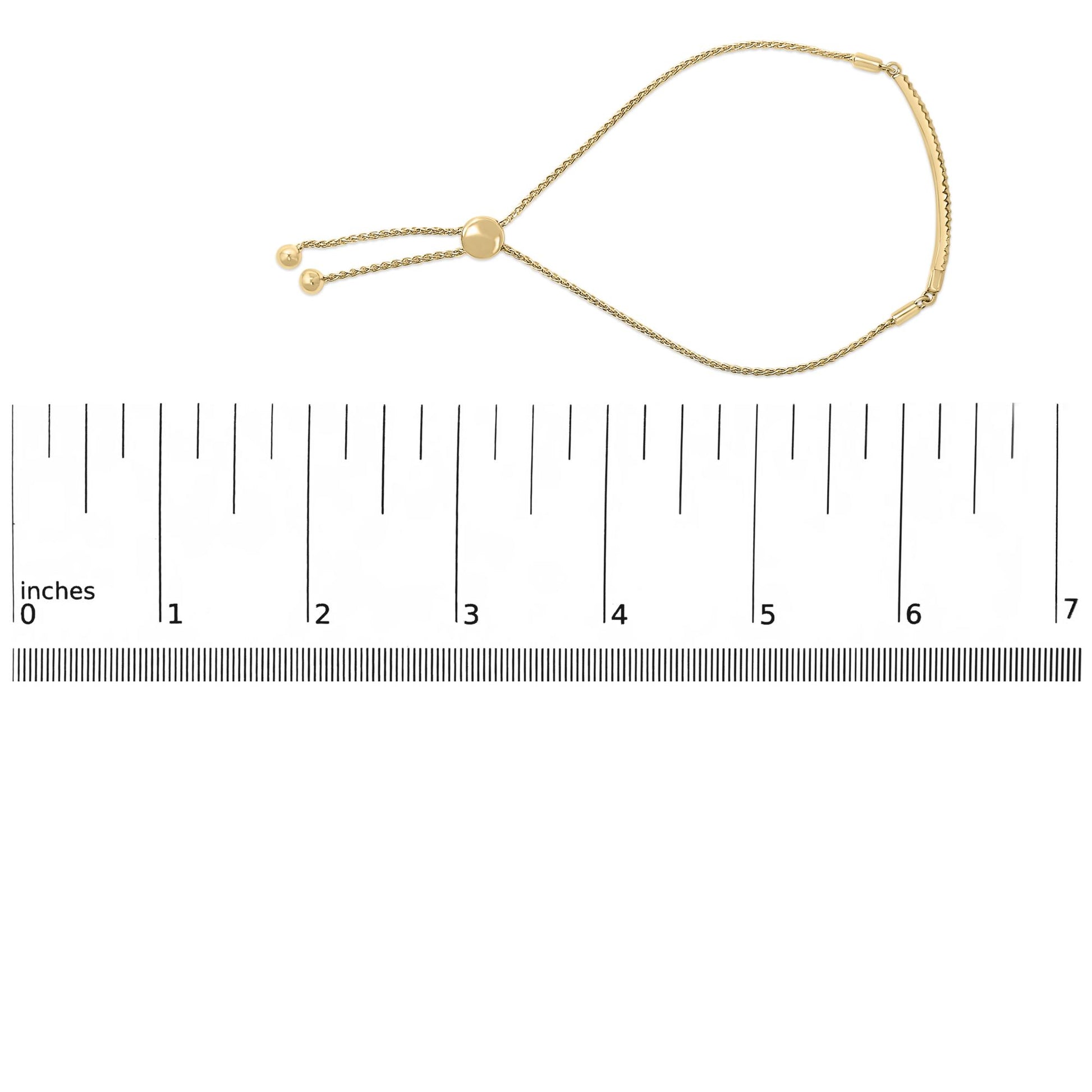 Yellow metal bracelet with round white gemstones in pave setting, shown flat on a ruler, photographed from above at a slight angle.