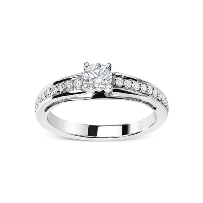 Front angle of a white metal ring featuring one round white gemstone in a four-prong setting and multiple smaller round white gemstones in shared prong settings along the band.
