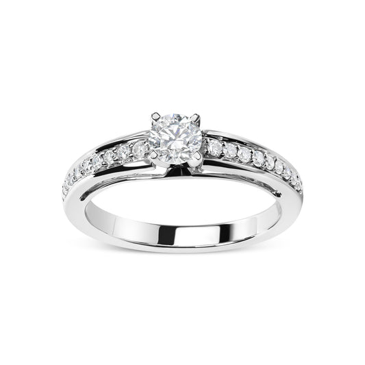 Front angle of a white metal ring featuring one round white gemstone in a four-prong setting and multiple smaller round white gemstones in shared prong settings along the band.