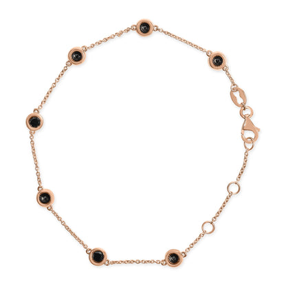 Top-down view of a rose-colored bracelet with a delicate chain featuring round black gemstones in bezel settings evenly spaced along the chain, including a lobster clasp closure.