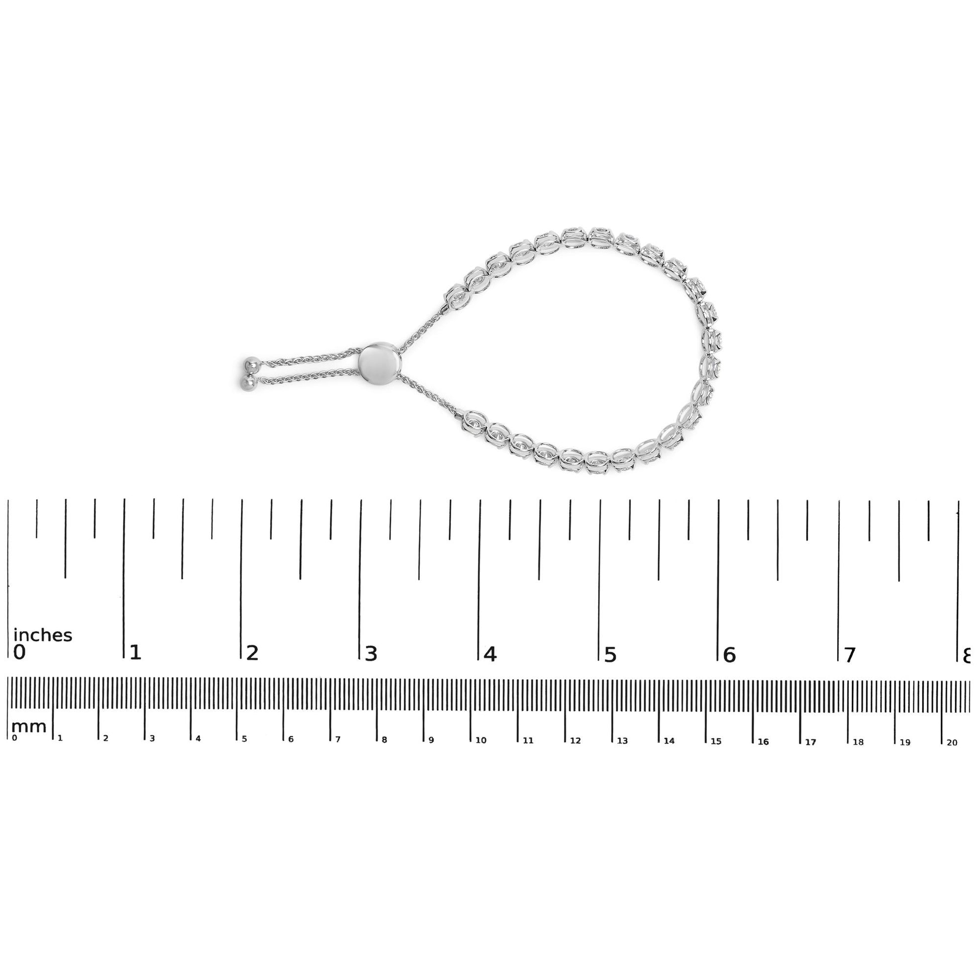 White metal bracelet with round white gemstones in four-prong settings, shown flat on a ruler for size reference, top-down angle.