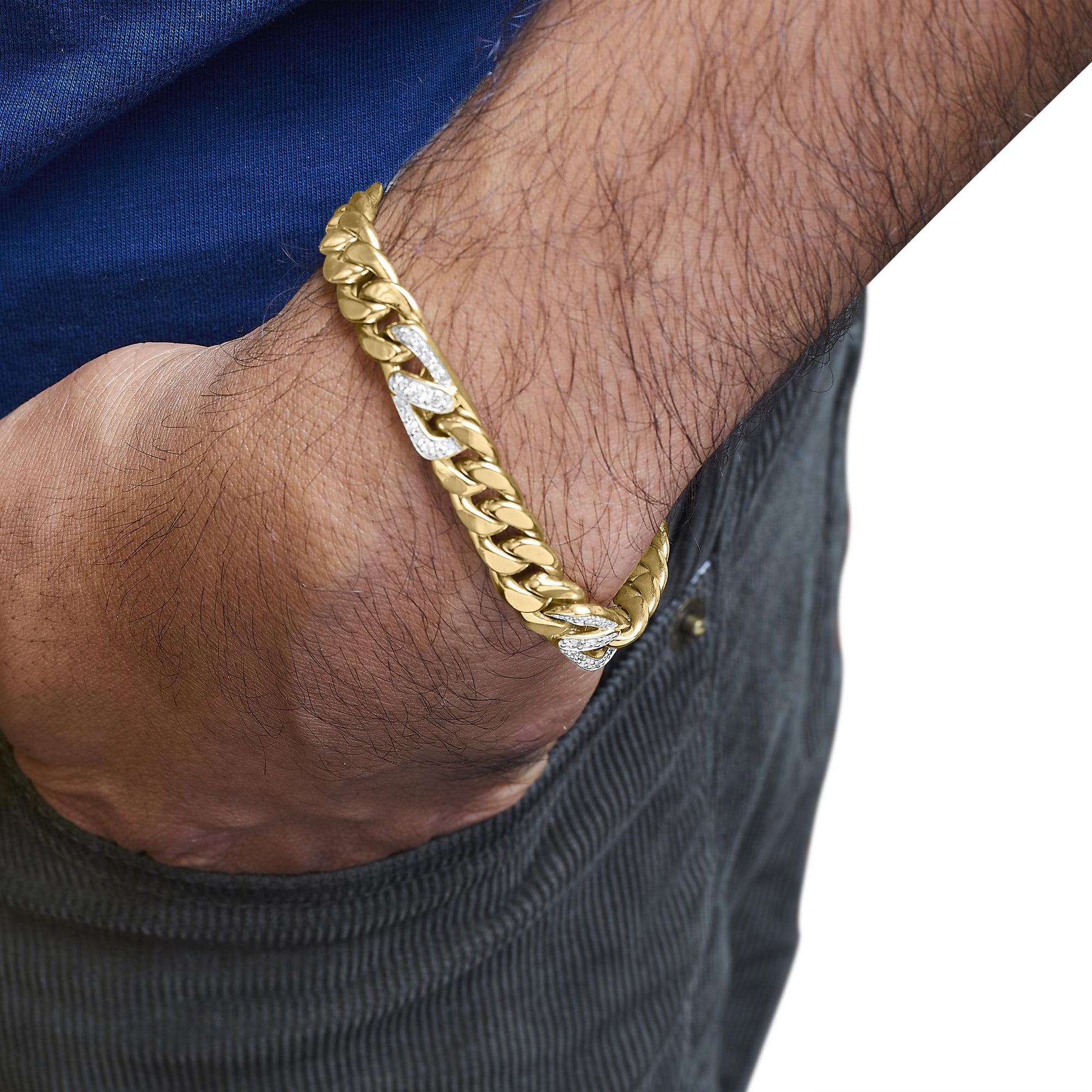 Yellow metal bracelet with large links, some links set with white round gemstones in shared prong setting, shown on a model's wrist from a side angle with their hand in a pocket.