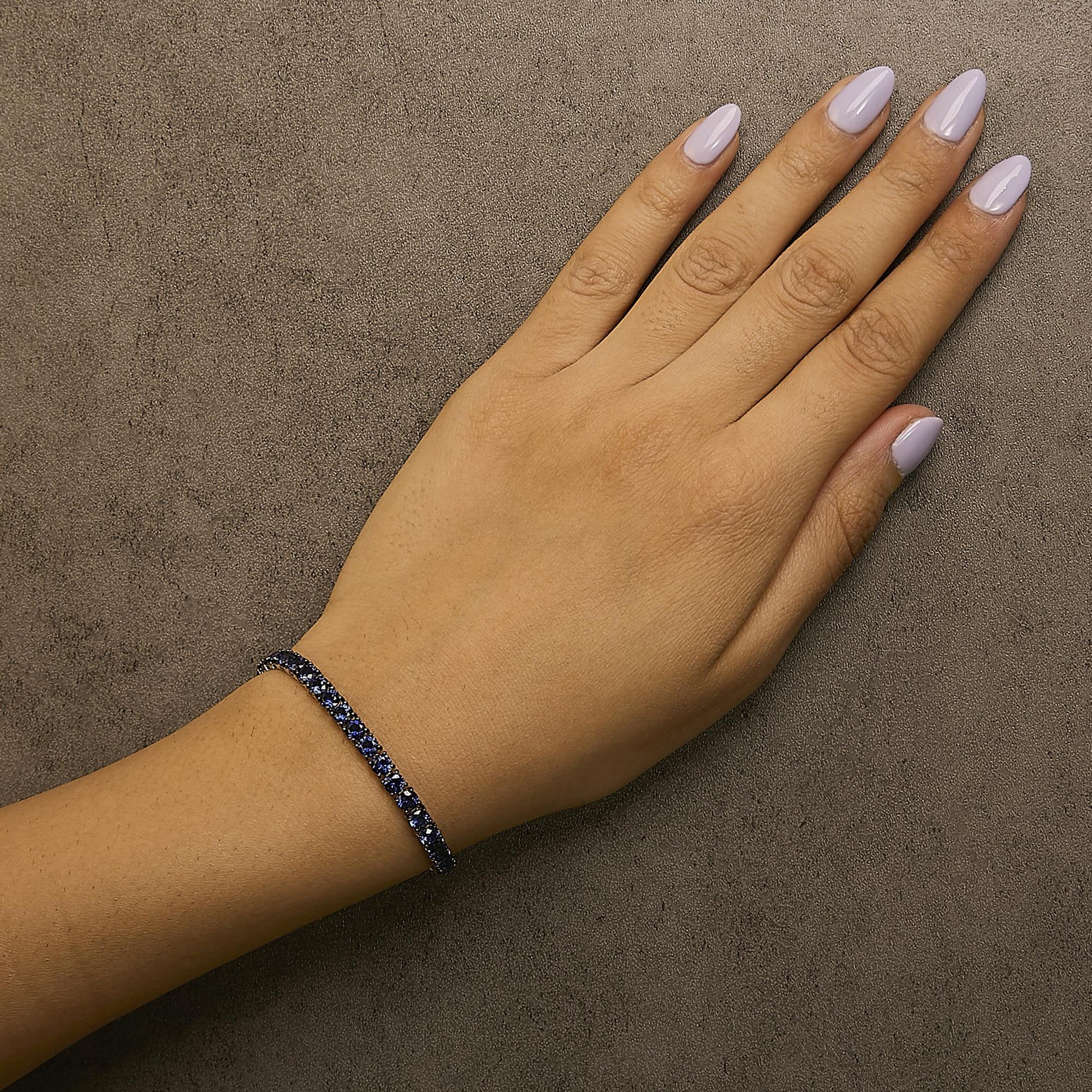 White bracelet with round blue gemstones in 4-prong settings shown worn on model's wrist, top-down angle.