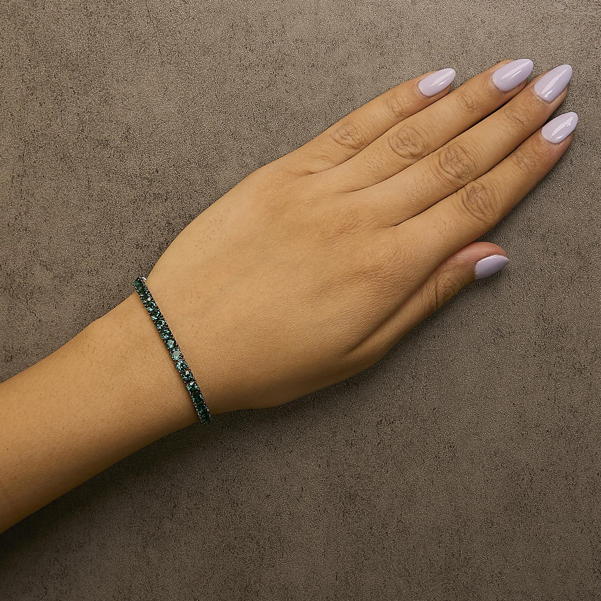 White bracelet with round green gemstones in 4-prong settings shown worn on a model's wrist, angled top-down.