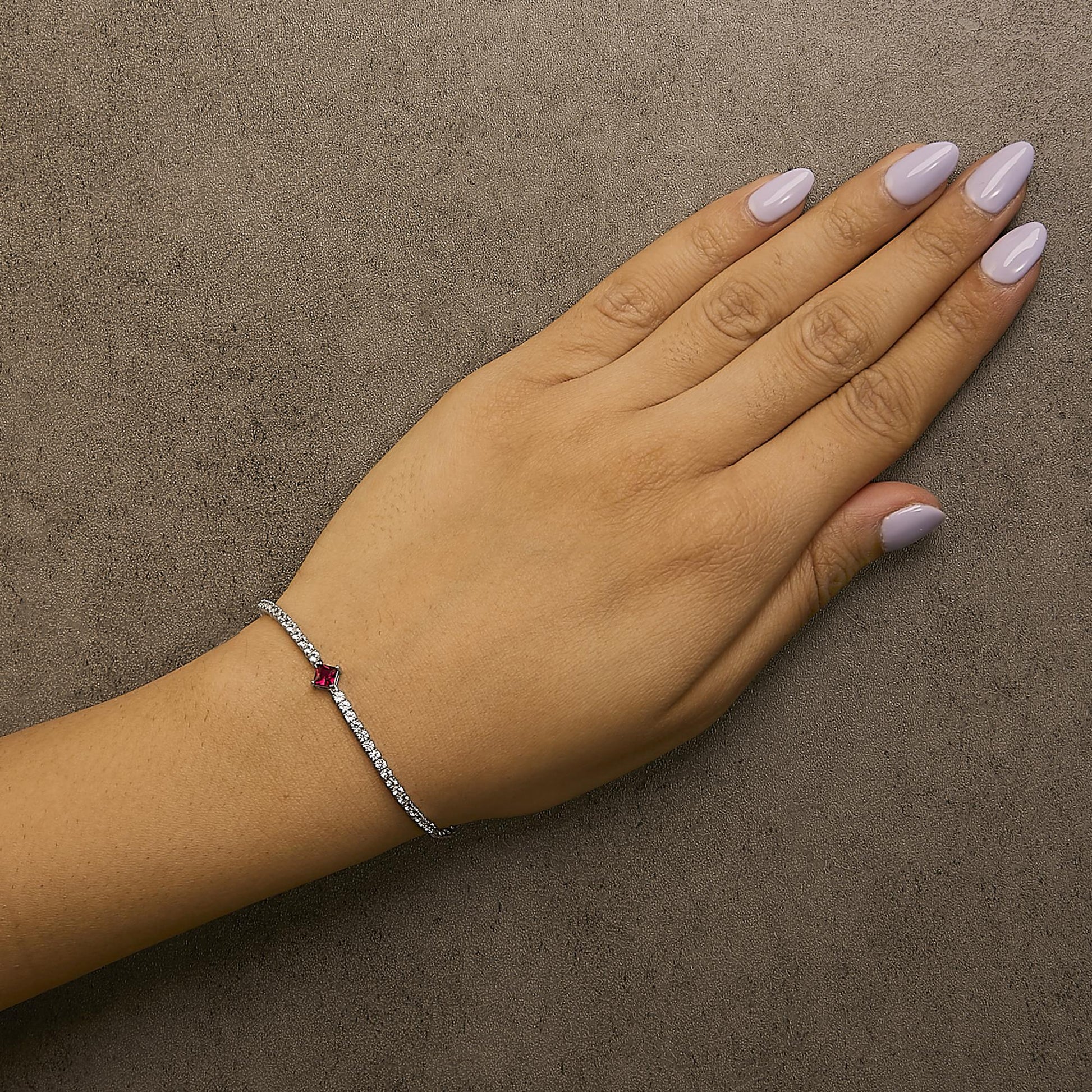 White metal bracelet with round white gemstones and a single princess-shaped red gemstone, shown worn on a model's wrist from a top angle.