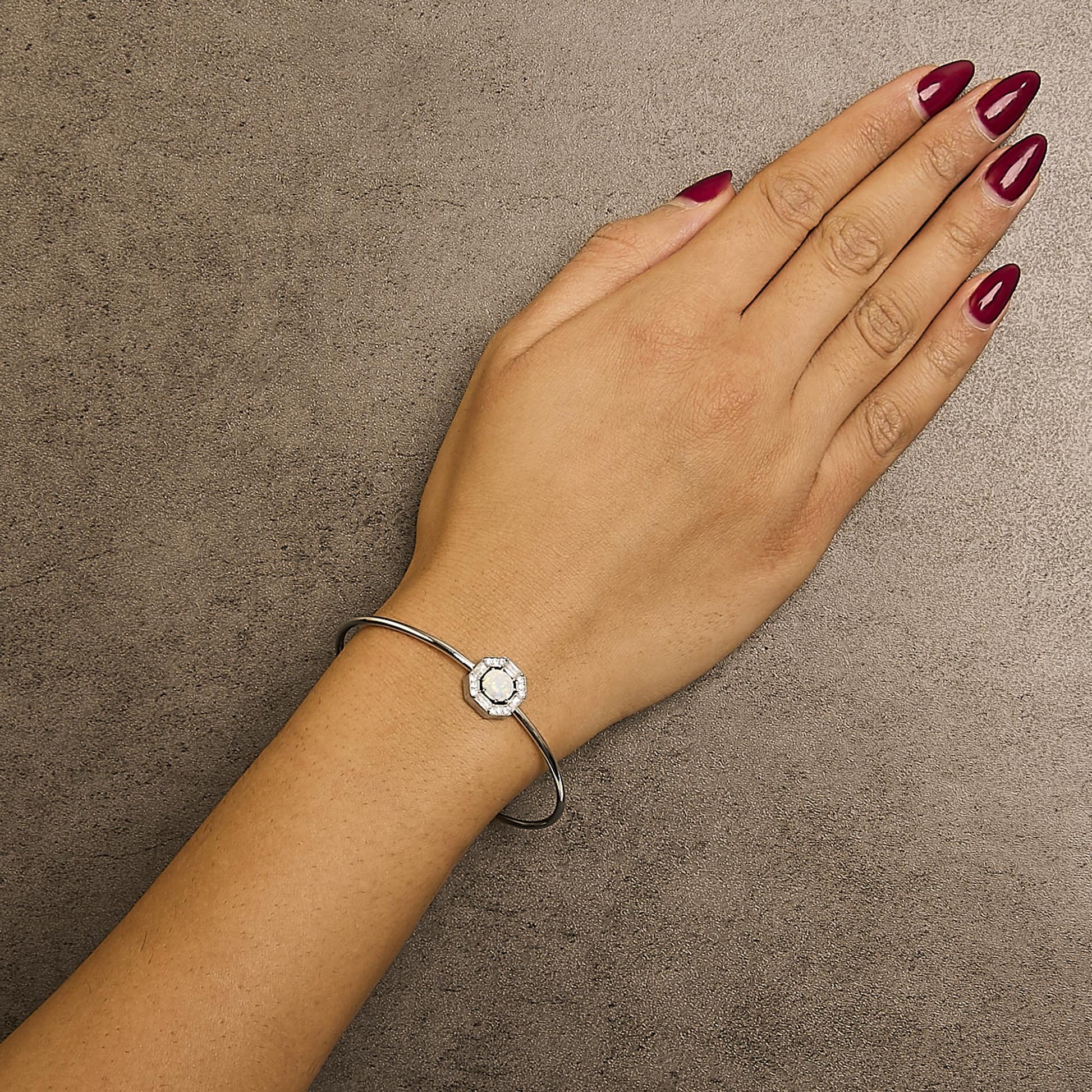 White metal bracelet with a central octagonal design featuring a round white opal gemstone surrounded by small round and baguette white gemstones, shown worn on a model's wrist, top-down angle.