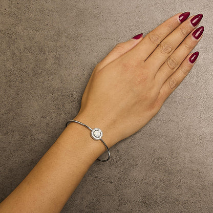 White metal bracelet with a central octagonal design featuring a round white opal gemstone surrounded by small round and baguette white gemstones, shown worn on a model's wrist, top-down angle.